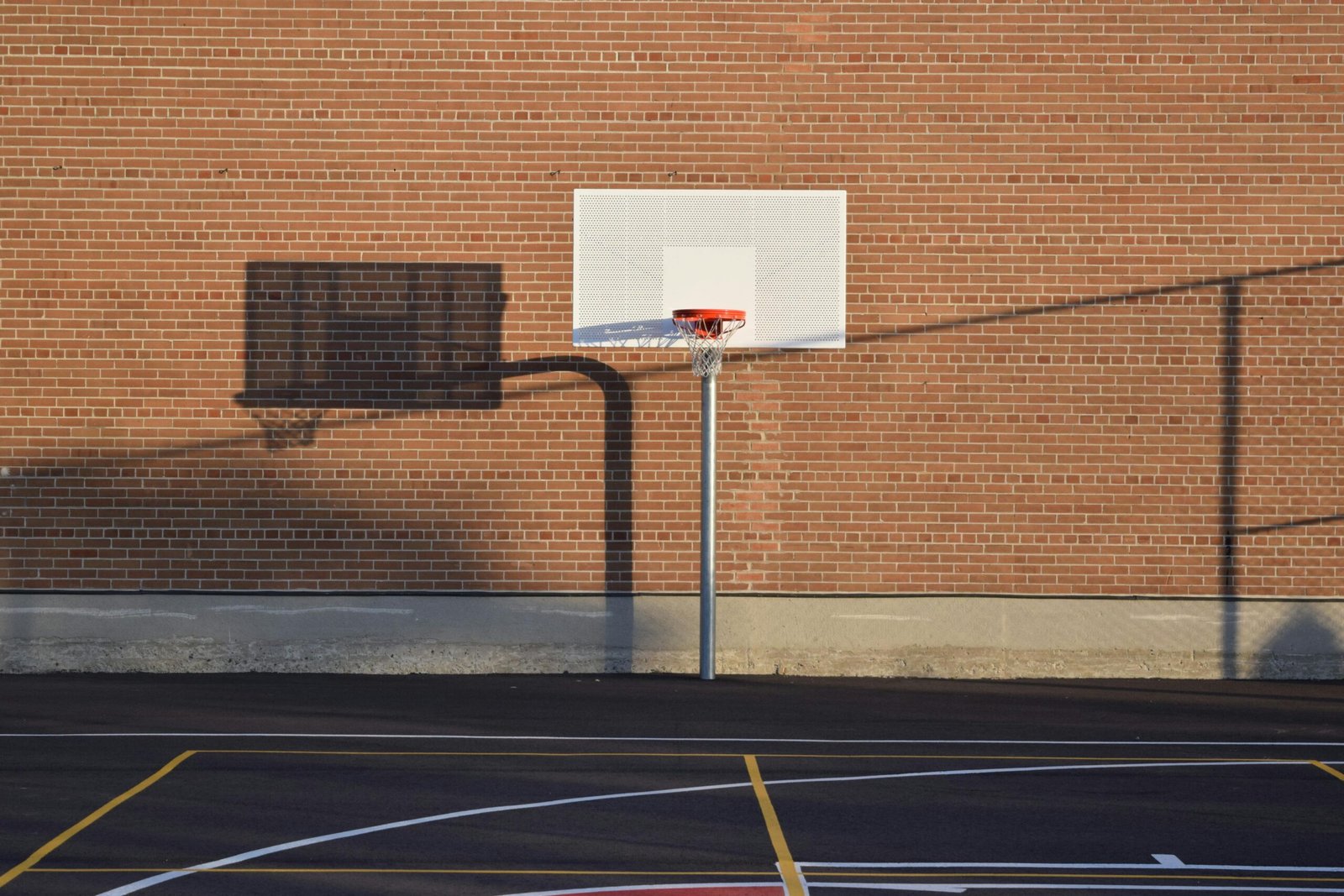 Home Empty outdoor basketball court with hoop and shadow against brick wall